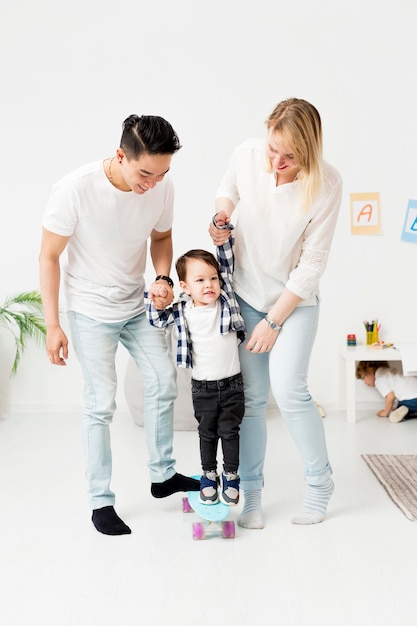 Free photo man and woman helping toddler using skatebord