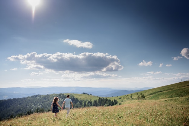 Man and woman hold their hands together walking on the hill somewhere in the mountains