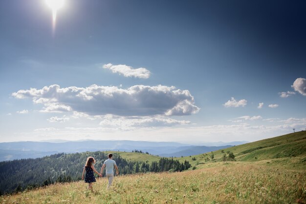 Man and woman hold their hands together walking on the hill somewhere in the mountains