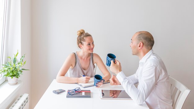 Мужчина и женщина с голубой керамической чашкой кофе, обсуждая на рабочем месте