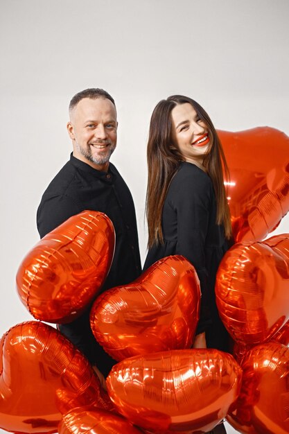 Man and woman holding bunch of heartshaped red ballons and posing in studio