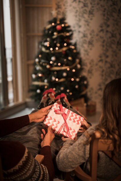 Man and woman holding gift box on chairs near Christmas tree