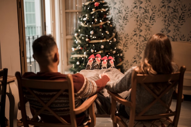 Free photo man and woman holding hands on chairs near christmas tree