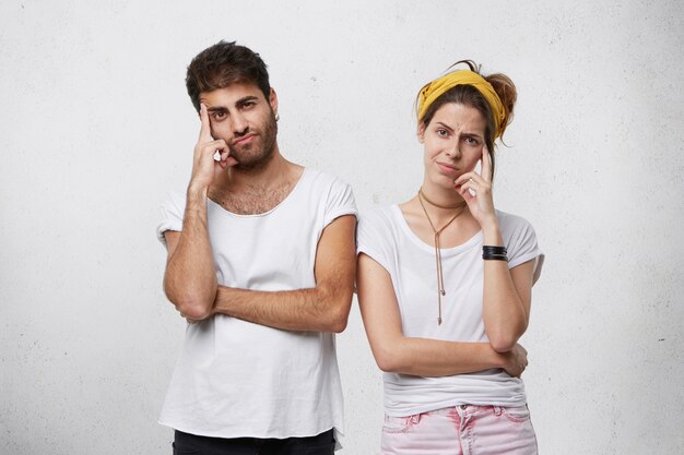 man and woman holding their fingers on temples reflecting closely about something while. Bearded guy standing near his wife thinking over their future plans