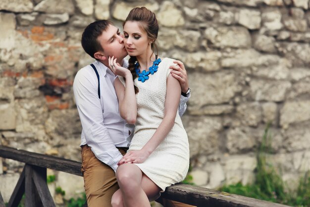 Мужчина и женщина целуют друг друга, нежно сидят на деревянных поручнях