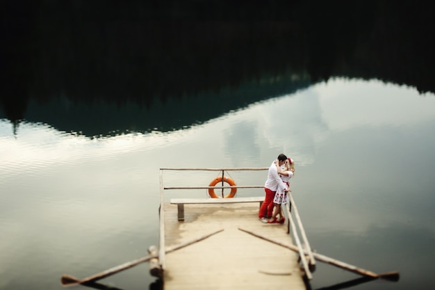Мужчина и женщина целуются на деревянном крыльце над горным озером
