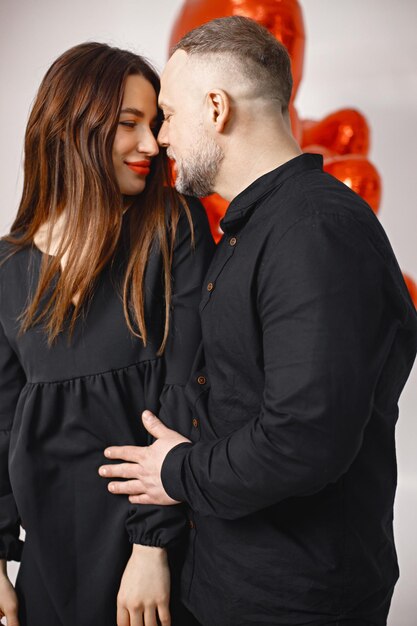 Man and woman kissing near bunch of heartshaped red ballons