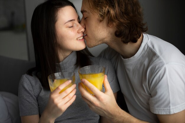 Man and woman kissing while holding glasses with orange juice