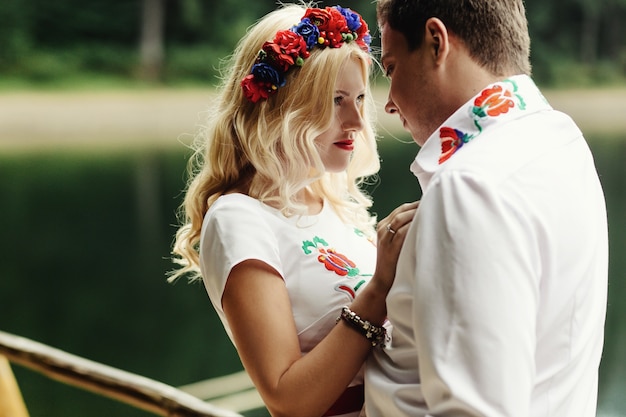 Man and woman lean to each other heads standing on wooden porch over mountain lake