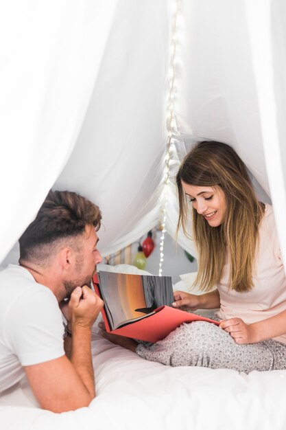 Man and woman looking at photo album sitting on bed under the white curtain