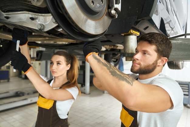 Man and woman mechanics repairing car undercarriage.