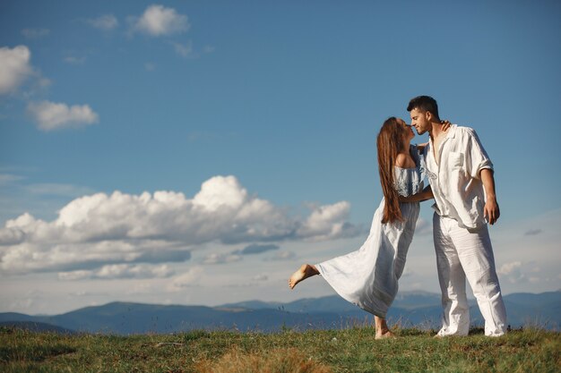 山の中の男と女。日没で恋をしている若いカップル。青いドレスを着た女性。空の背景に立っている人々。