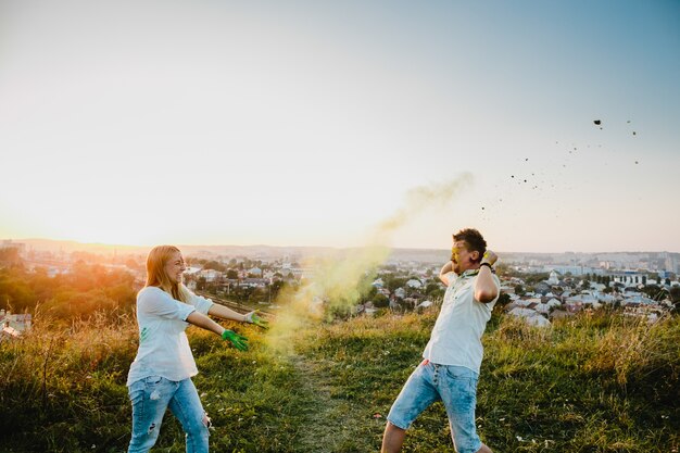 Man and woman play with colorful smoke standing on the green lawn