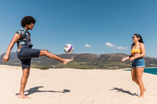 Free photo man and woman playing soccer on sand beach