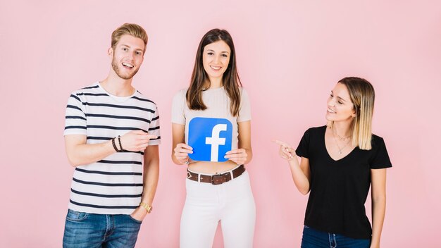 男性と女性は、ピンクの背景にFacebookのアイコンを保持している彼らの友人を指して