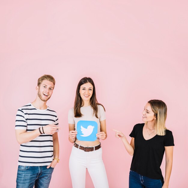 Man and woman pointing at their friend holding twitter icon on pink background