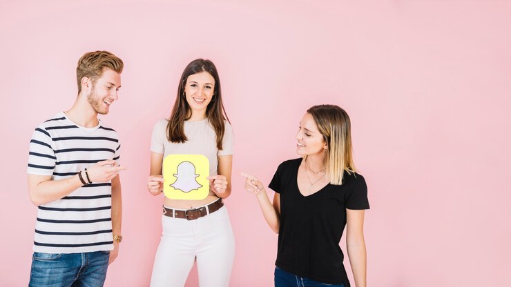 Free Photo man and woman pointing at their happy friend holding snapchat icon