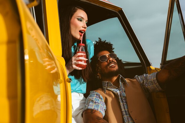 Мужчина и женщина позируют в стиле ретро с автомобилем и напитком