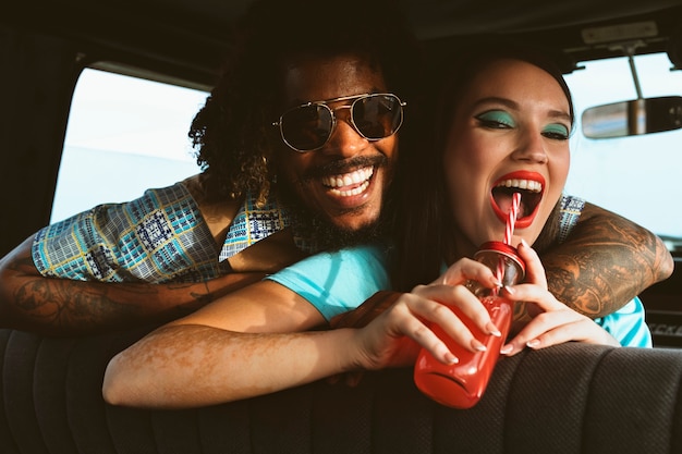 Man and woman posing together in retro style inside vehicle with juice