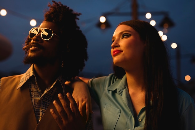 Man and woman posing together in retro style at night with lights