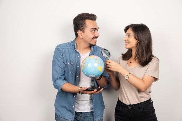 Man and woman posing with globe on white.