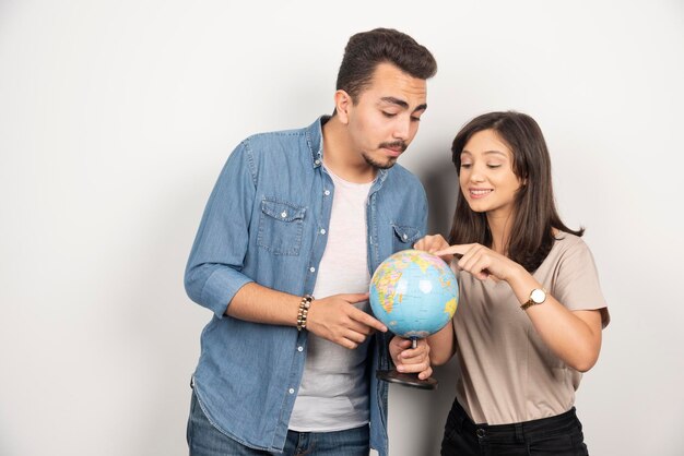 Man and woman posing with globe on white.