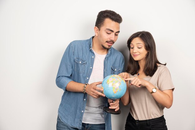 Man and woman posing with globe on white.