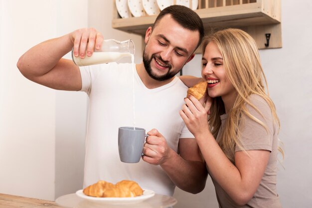 Man and woman pouring milk and eating croissants