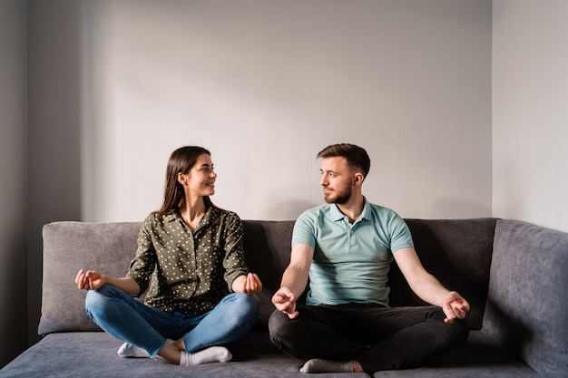 Free photo man and woman sitting on sofa in lotus pose