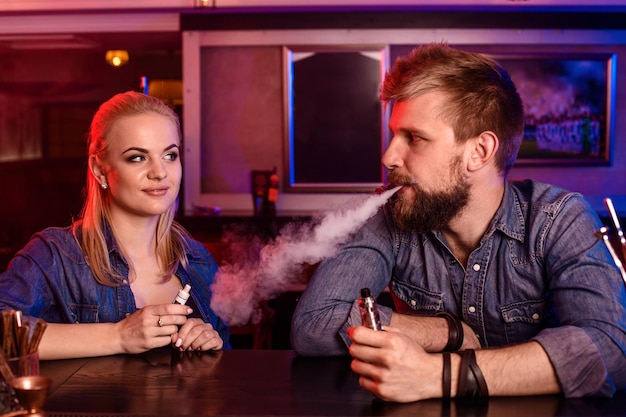 Free photo a man and woman smoking electronic cigarette in a vape bar.