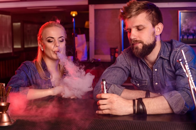 Free photo a man and woman smoking electronic cigarette in a vape bar.