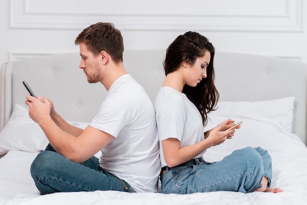 Мужчина и женщина остаются в спине, проверяя свои телефоны
