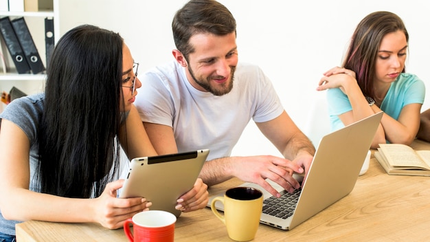 Man and woman using electronic gadgets sitting near their friend reading book