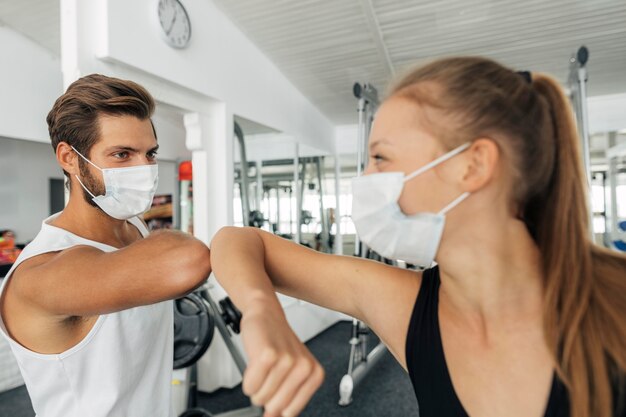 Man and woman with medical masks doing the elbow salute at the gym