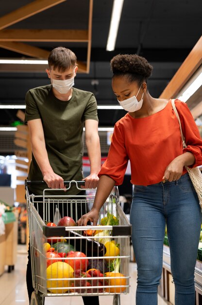 Man and woman with medical masks out grocery shopping with shopping cart