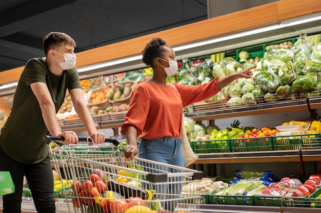 医療マスクを持つ男性と女性は、ショッピングカートで食料品の買い物をします