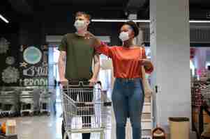 Free photo man and woman with medical masks out grocery shopping with shopping cart