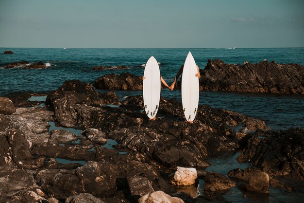 Man and woman with surf boards holding hands on stone coast