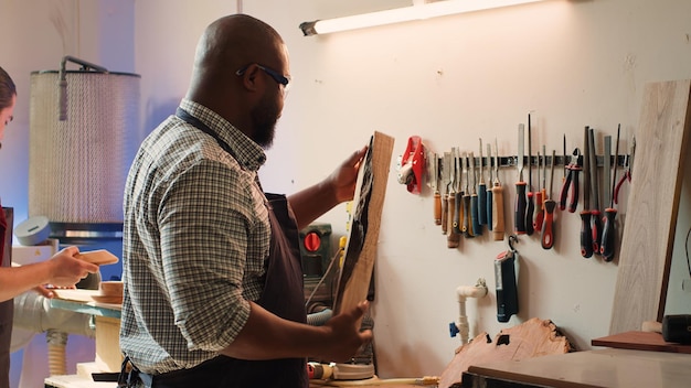 Foto gratuita uomo in un'officina di lavorazione del legno che ispeziona un pezzo di legno prima di assemblare i mobili