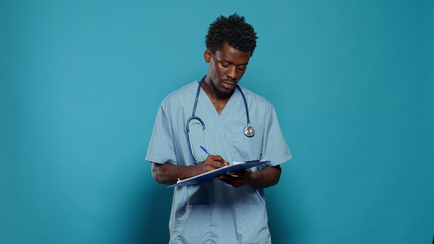 Free photo man working as nurse and writing on medical paper. healthcare specialist with uniform and stethoscope taking notes about disease and lifestyle, standing over isolated background.