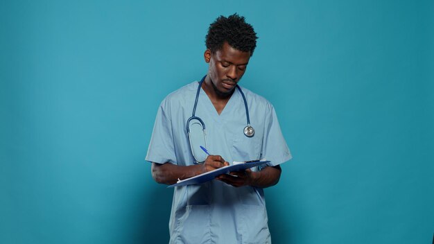 Man working as nurse and writing on medical paper. Healthcare specialist with uniform and stethoscope taking notes about disease and lifestyle, standing over isolated background.