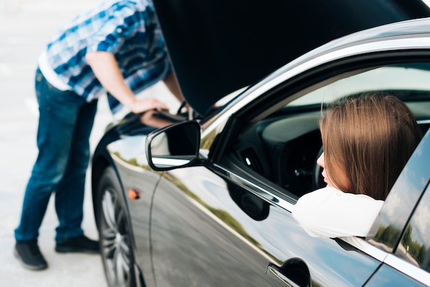 Man working on engine and woman sitting in car