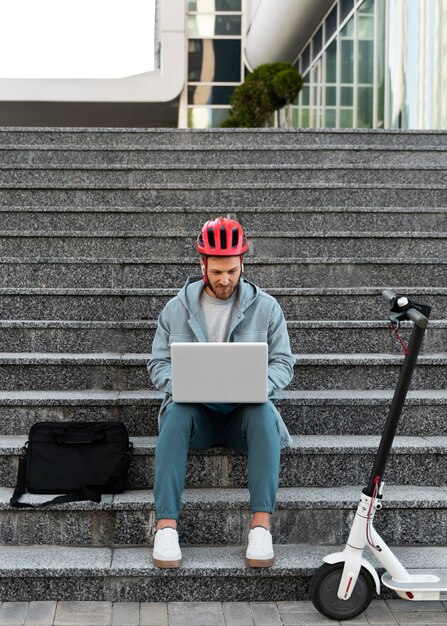 彼のスクーターの隣に彼のラップトップで働いている男