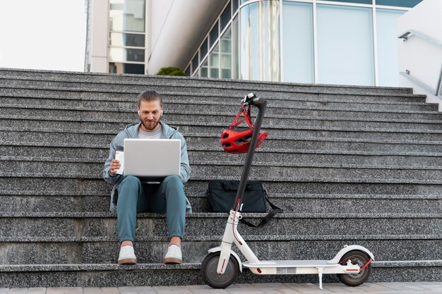 Man working on his laptop next to his scooter