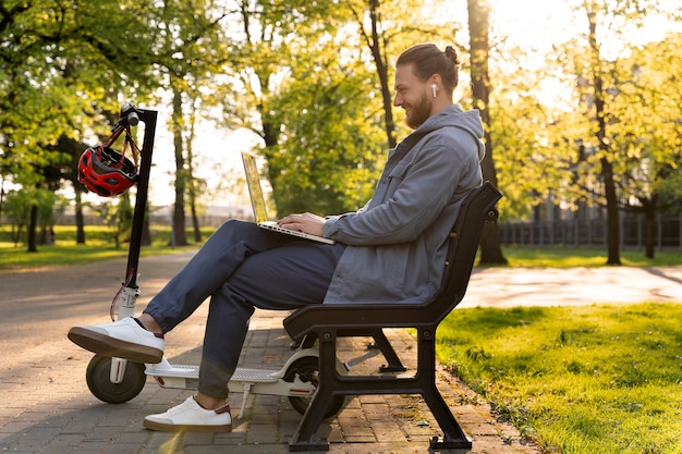 Foto gratuita uomo che lavora sul suo laptop accanto al suo scooter