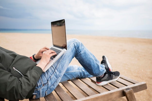 Uomo che lavora al computer portatile sulla sedia di spiaggia