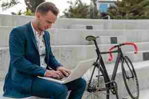 Free photo man working on laptop next to his bike outdoors