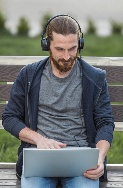 Uomo che lavora al computer portatile con le cuffie all'aperto