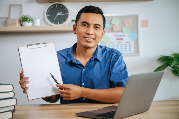 Man working in office holding papers with laptop on desk