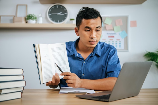 Man working in office holding papers with laptop on desk